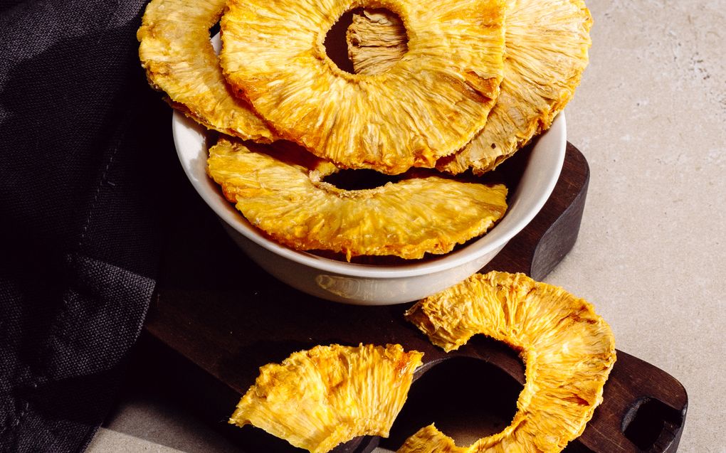 Dehydrated pineapple rings in a bowl on a dark wooden board